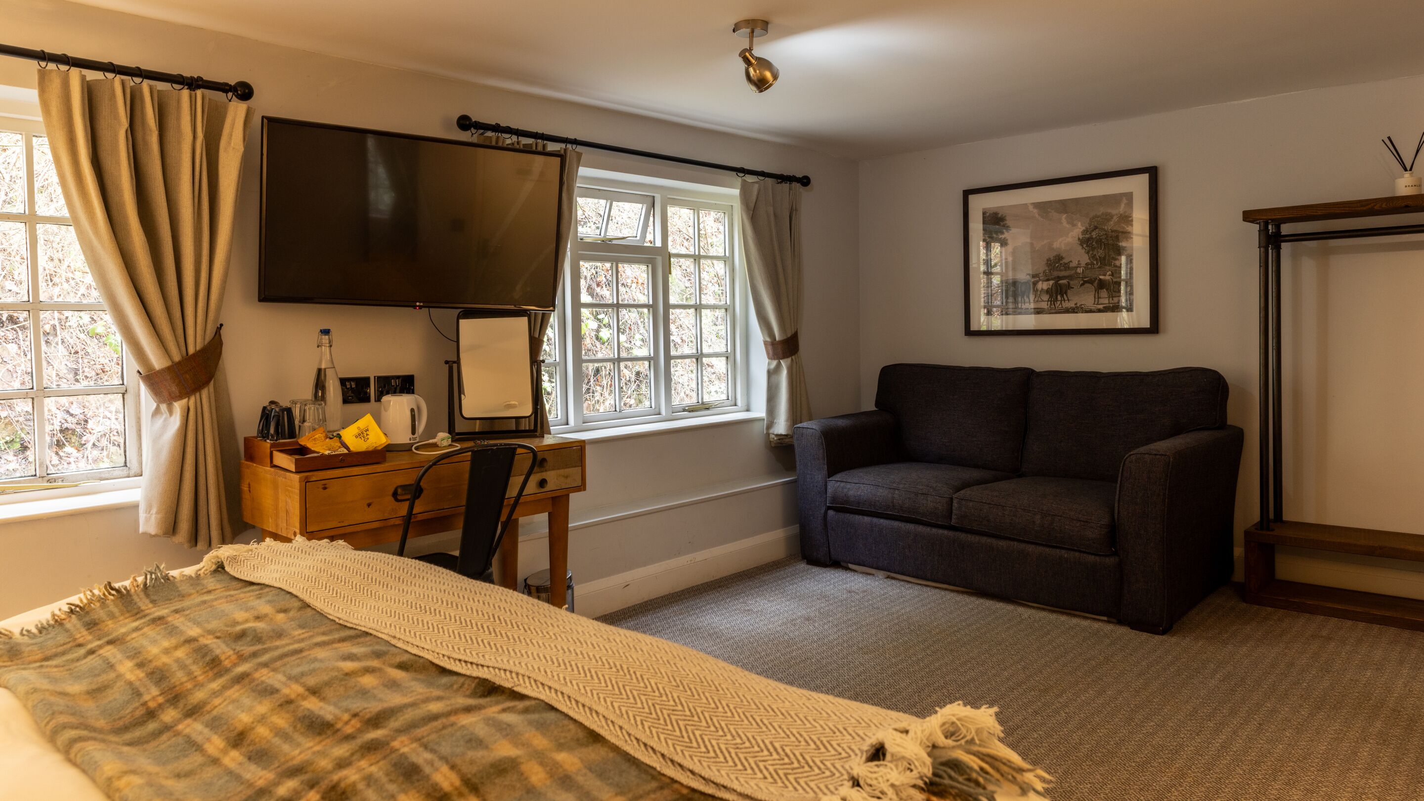 Une chambre à coucher avec un lit, un bureau avec un ordinateur, un canapé et une fenêtre avec des rideaux.