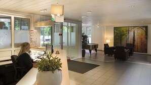 Un vestíbulo de hotel moderno con mostrador de recepción, zona de estar y un cuadro grande de un bosque.