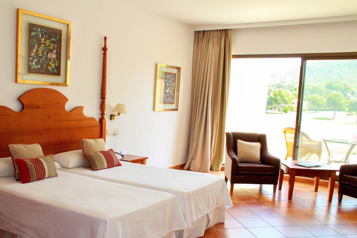 Une chambre d’hôtel avec deux lits, une tête de lit en bois, une chaise, une table et une vue sur l’extérieur.