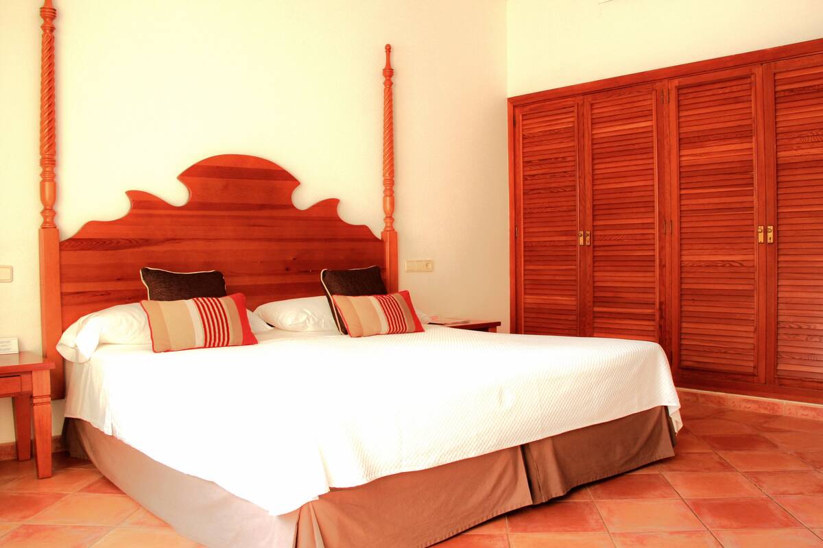 Une chambre à coucher avec un lit en bois, deux tables de chevet, une petite table et une grande armoire en bois.
