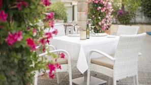 A white wicker table set outdoors with a white tablecloth, surrounded by chairs.