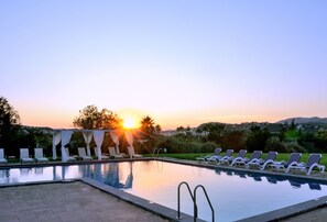 A pool with lounge chairs and a sunset in the background.