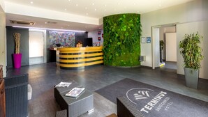 Zona de recepción de un hotel con diseño moderno, que incluye un mostrador de recepción, un área de estar y una pared verde con follaje.
