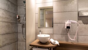 Un baño moderno con tocador de madera, un lavabo blanco, una toalla, un cabezal de ducha de mano y un espejo.