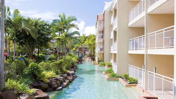 A hotel with a water feature, palm trees, and balconies.