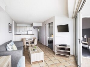 A modern apartment with a living room, dining area, kitchenette, and a bedroom with a sliding door. - BreakFree Alexandra Beach (Alexandra Headland)