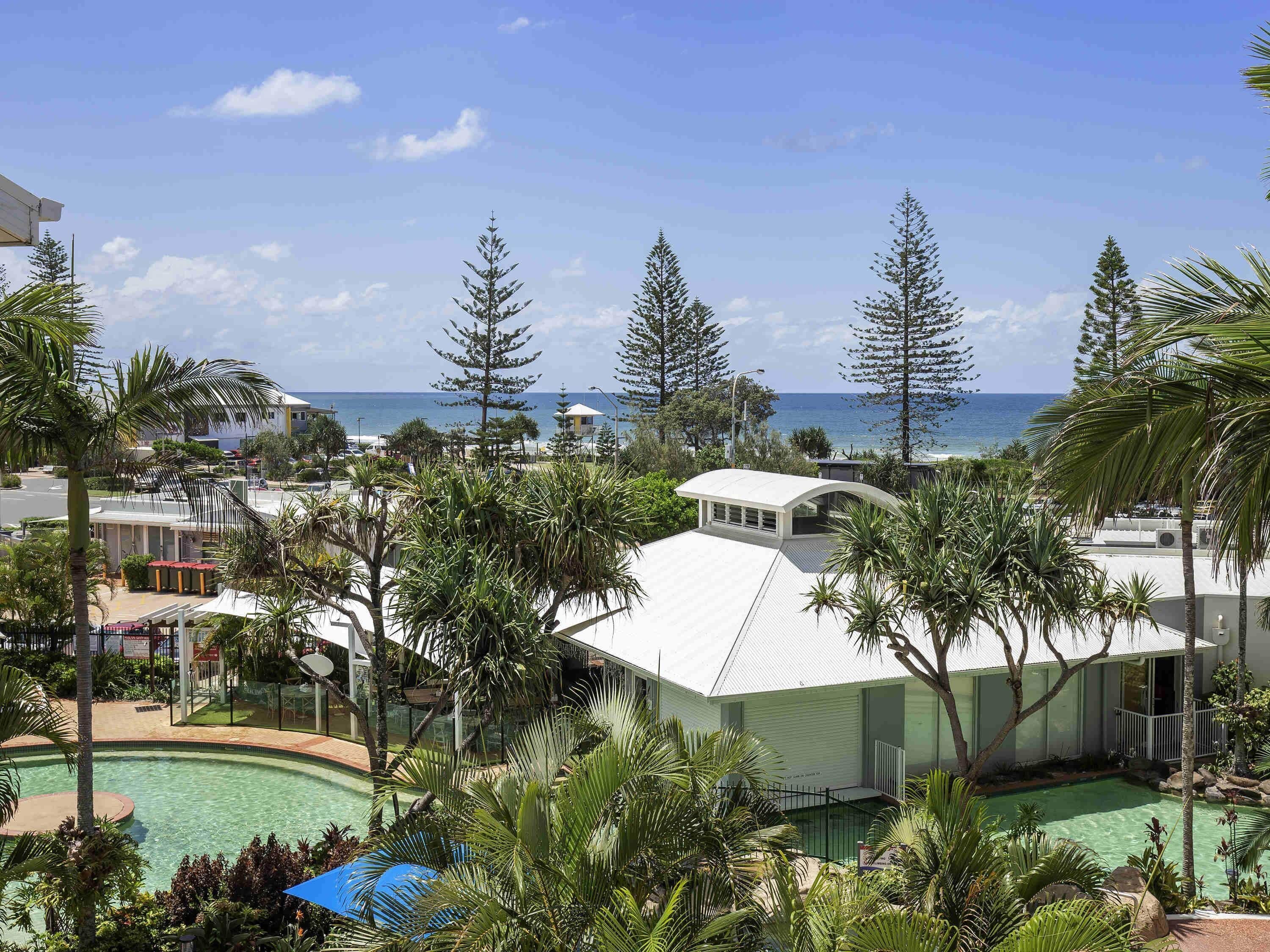 A resort with a pool, palm trees, and a view of the ocean.