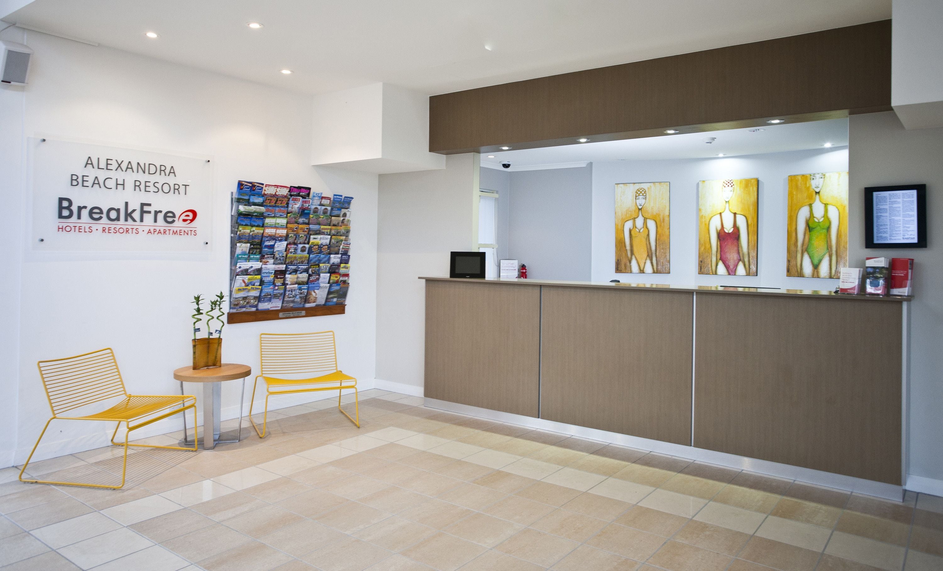A reception area with a bulletin board, two yellow chairs, a small table, and artwork on the wall.