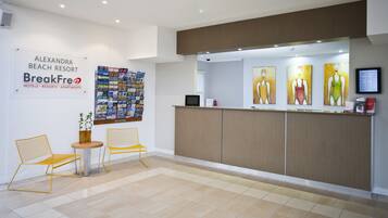 A reception area with a bulletin board, two yellow chairs, a small table, and artwork on the wall.