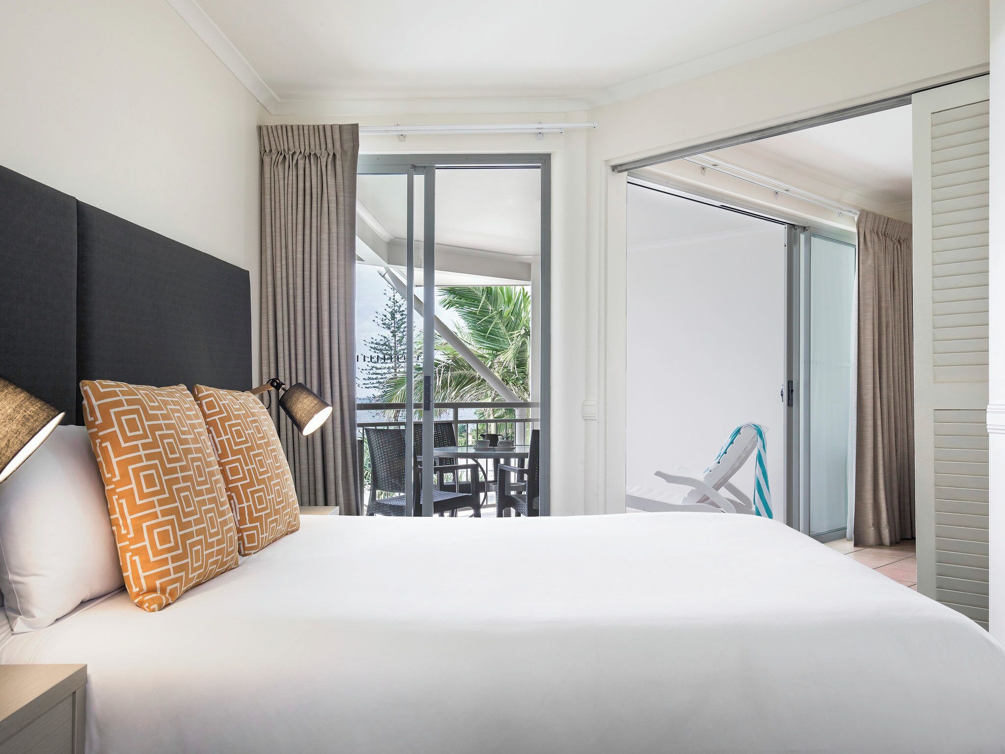 Une chambre d’hôtel avec un grand lit, un balcon doté d’une table et de chaises, et une vue sur la verdure.