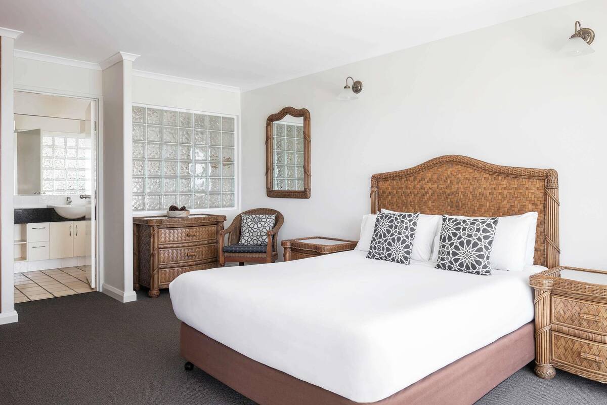 A bedroom with a large bed, a dresser, a chair, a mirror, and a window with frosted glass.
