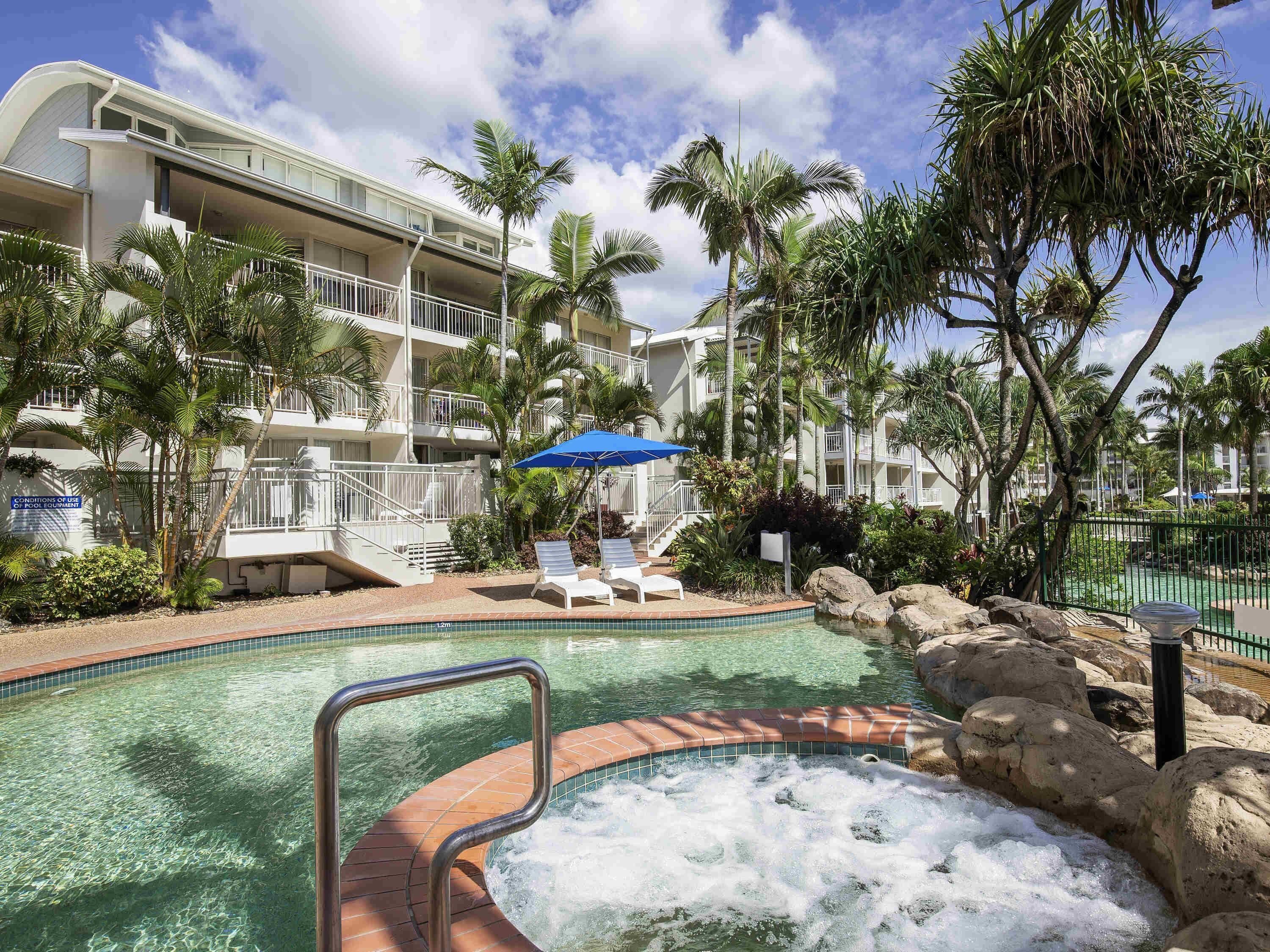 A hotel pool area with a hot tub, lounge chairs, and palm trees.