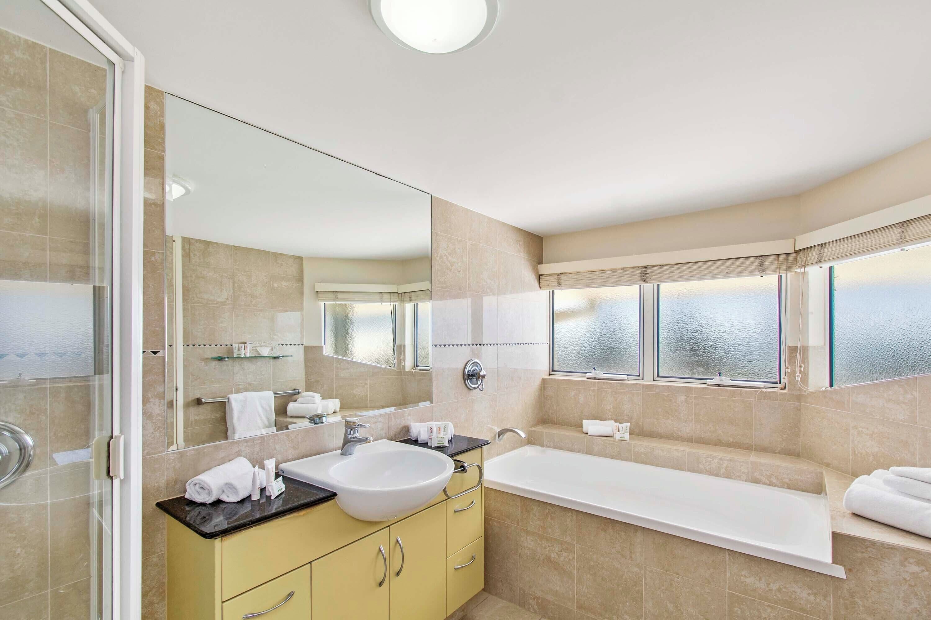 Une salle de bain moderne avec un grand miroir, un lavabo, une baignoire et une fenêtre en verre dépoli.