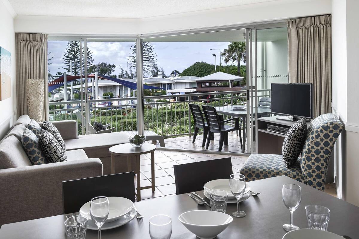 A hotel room with a balcony, a dining area, and a TV.
