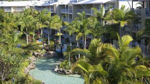 A resort with multiple-story buildings, a pool area with clear water, and lush palm trees.