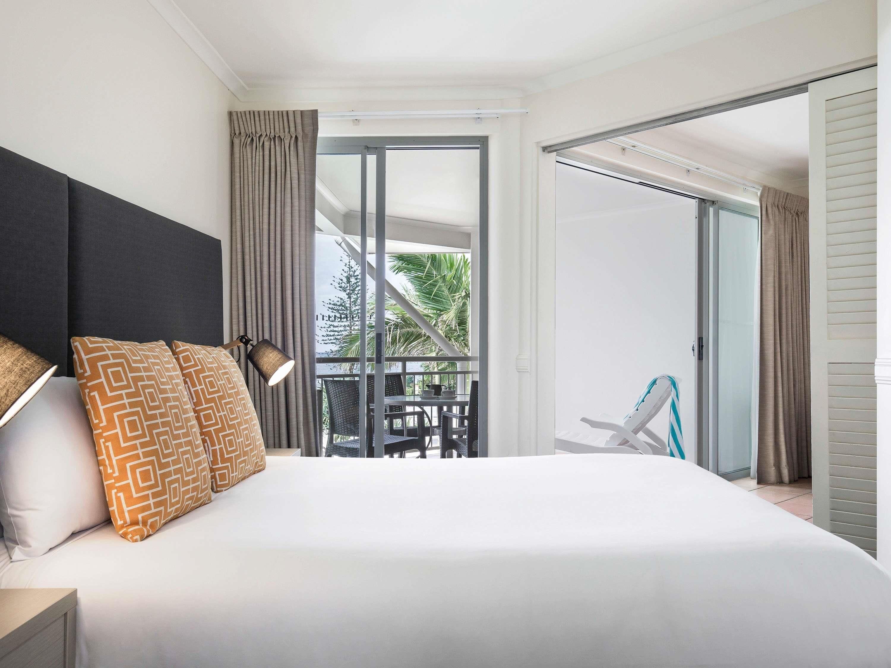 Une chambre d’hôtel avec un lit, une table de chevet, une lampe, un balcon avec une chaise et une vue sur la verdure.