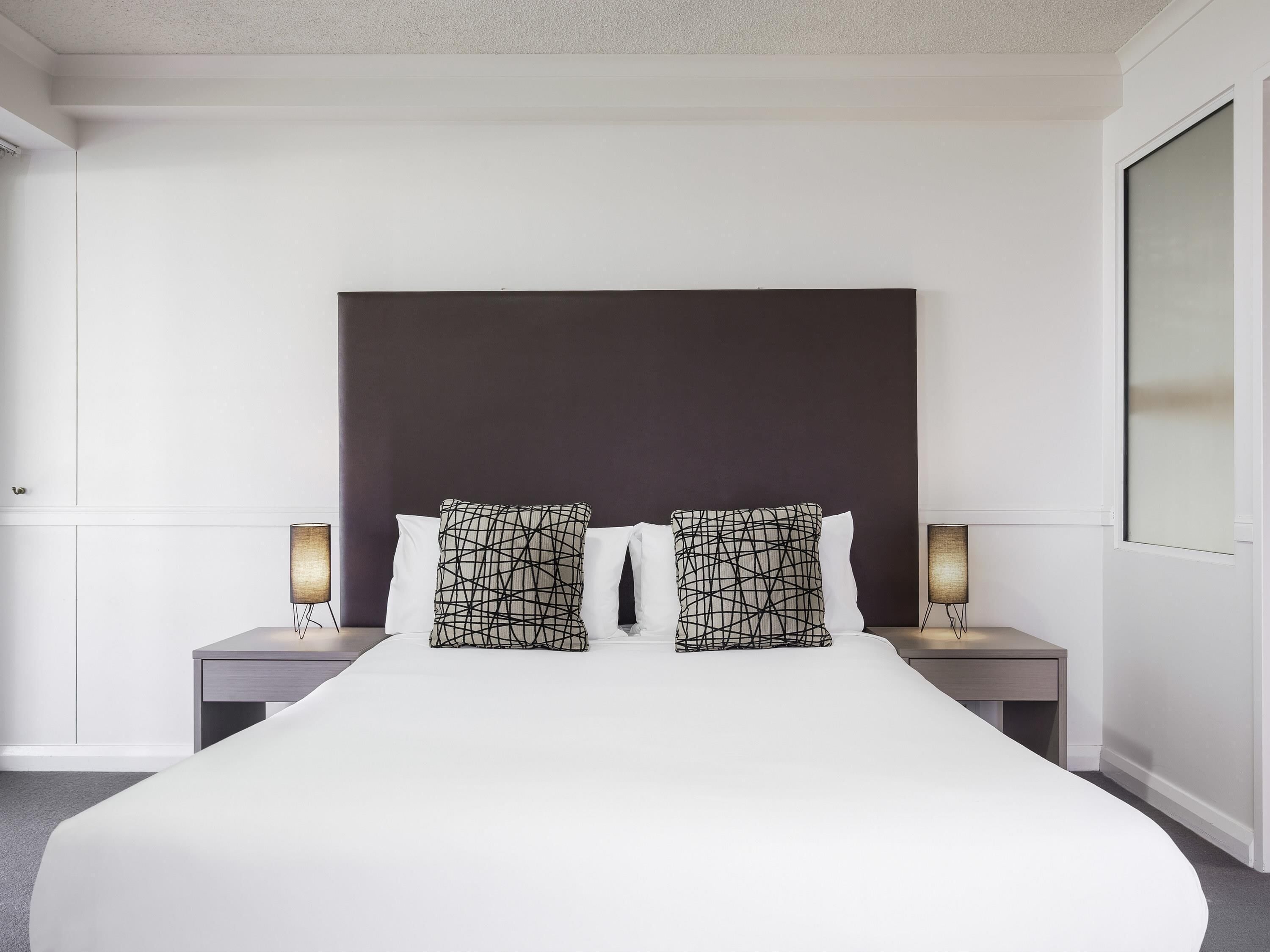 A hotel room with a large bed, two bedside tables with lamps, and a dark headboard.
