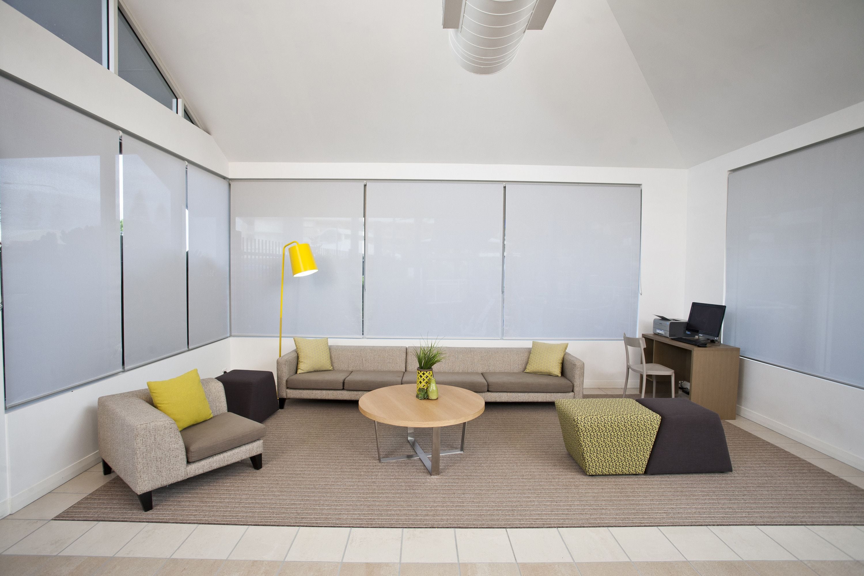 A modern living room with a sofa, armchair, coffee table, and a desk with a computer.