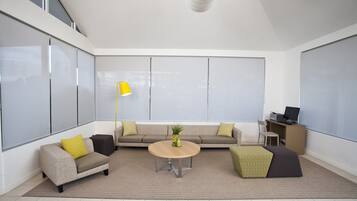 A modern living room with a sofa, armchair, coffee table, and a desk with a computer.