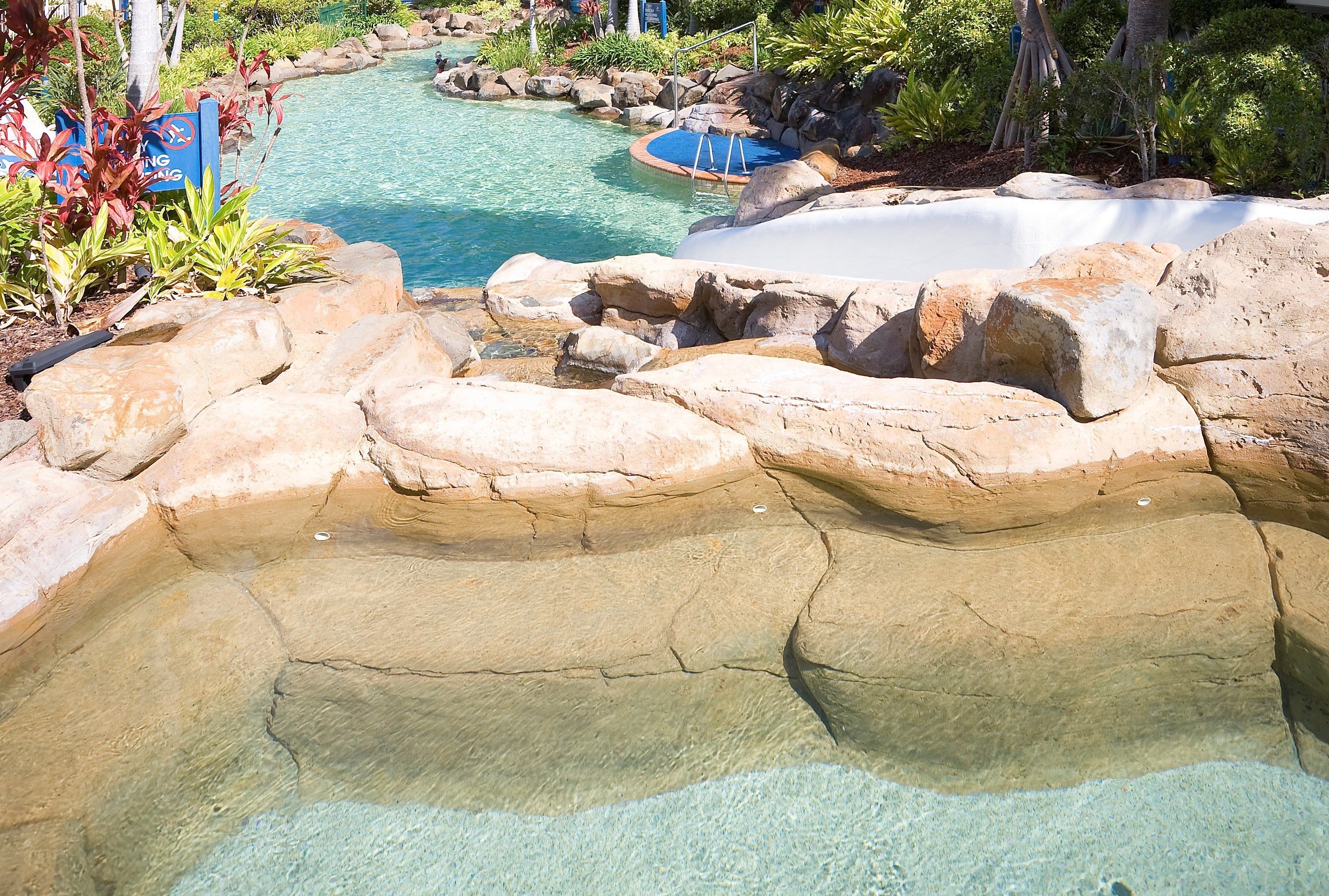 Ein Poolbereich mit klarem Wasser, umgeben von Felsen und Pflanzen.