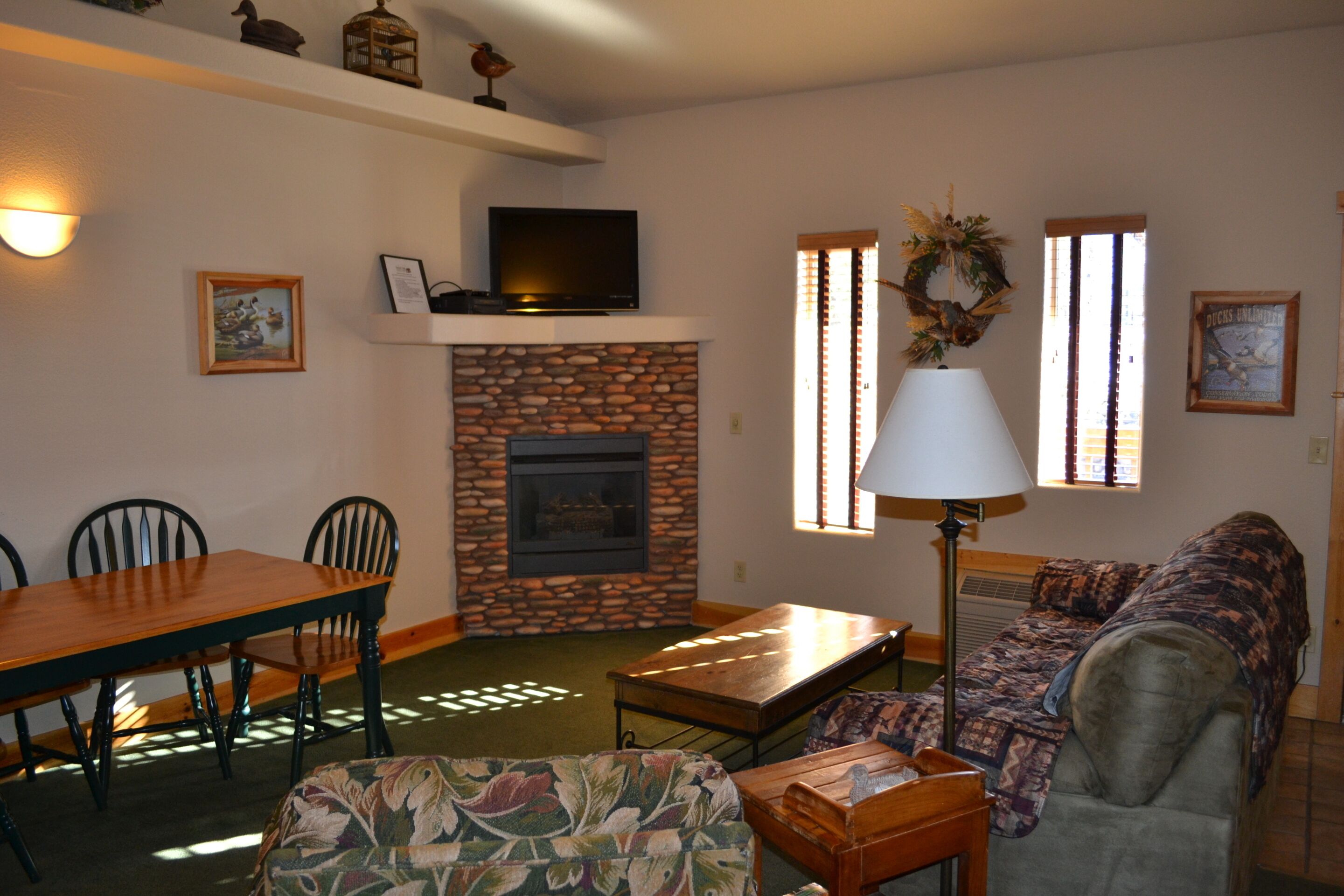 A living room with a fireplace, a television, a dining table with chairs, a sofa, and a lamp.