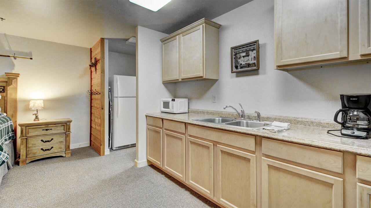 A compact kitchen with wooden cabinets, a microwave, a sink, and a coffee maker.