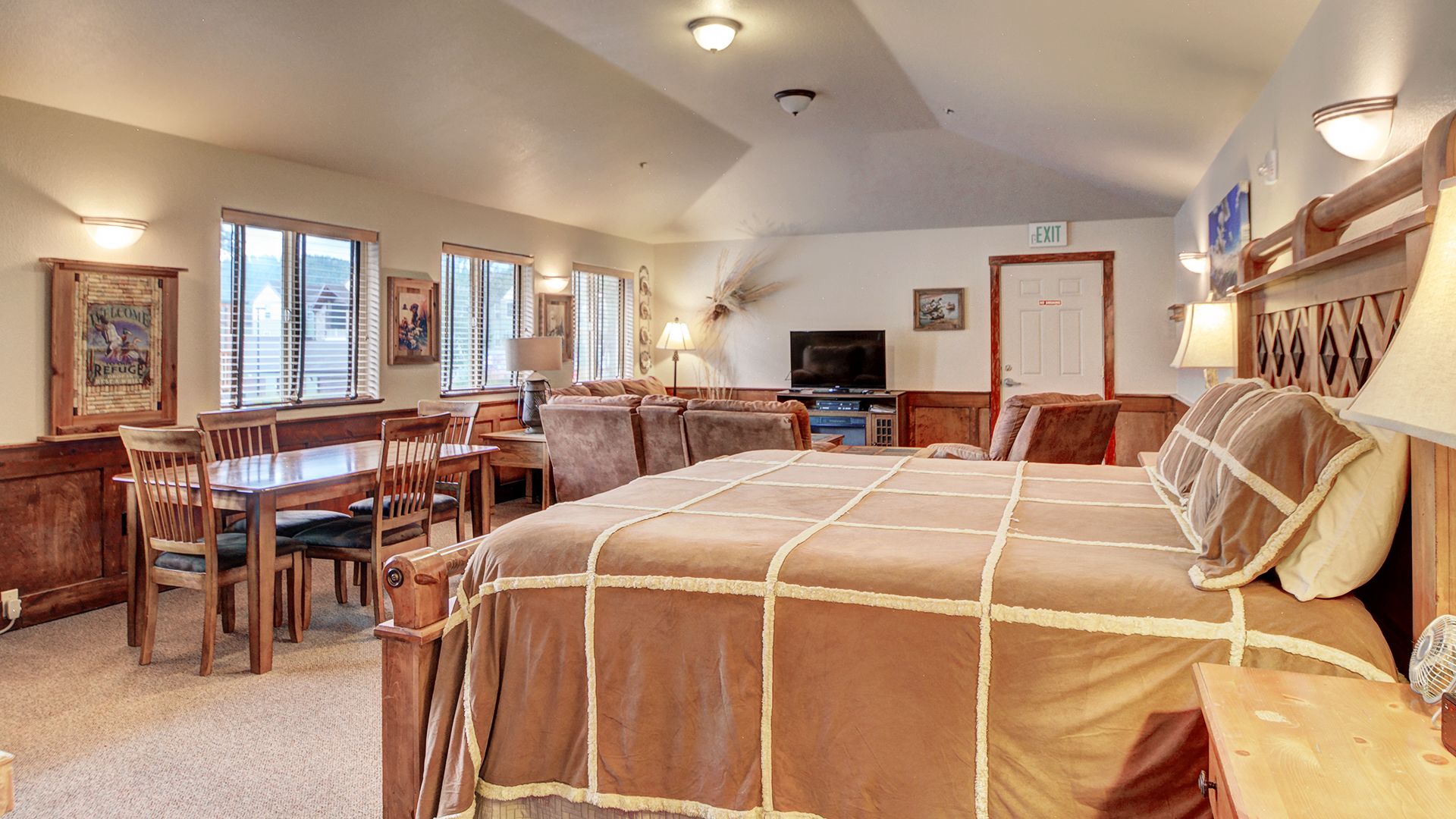 A spacious room with a large bed, a dining table, and multiple chairs. There is a television and a lamp on a side table.