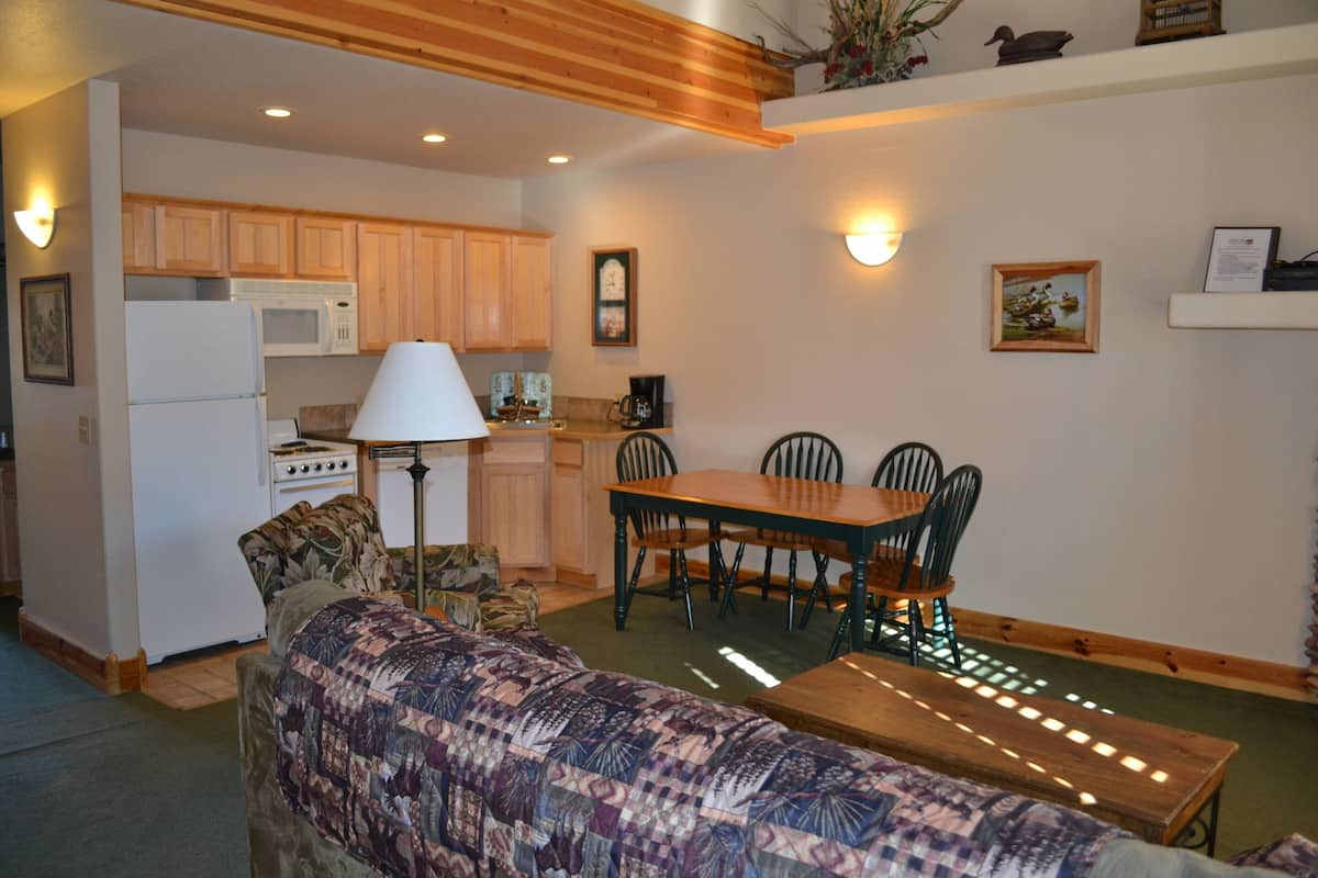 A cozy living room with a sofa, a dining table with chairs, a kitchen area with cabinets and appliances, and decorative wall lights.