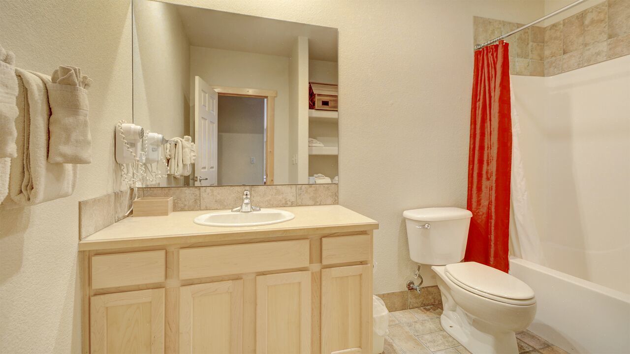 Un baño con lavamanos, espejo, inodoro y cortina de ducha.