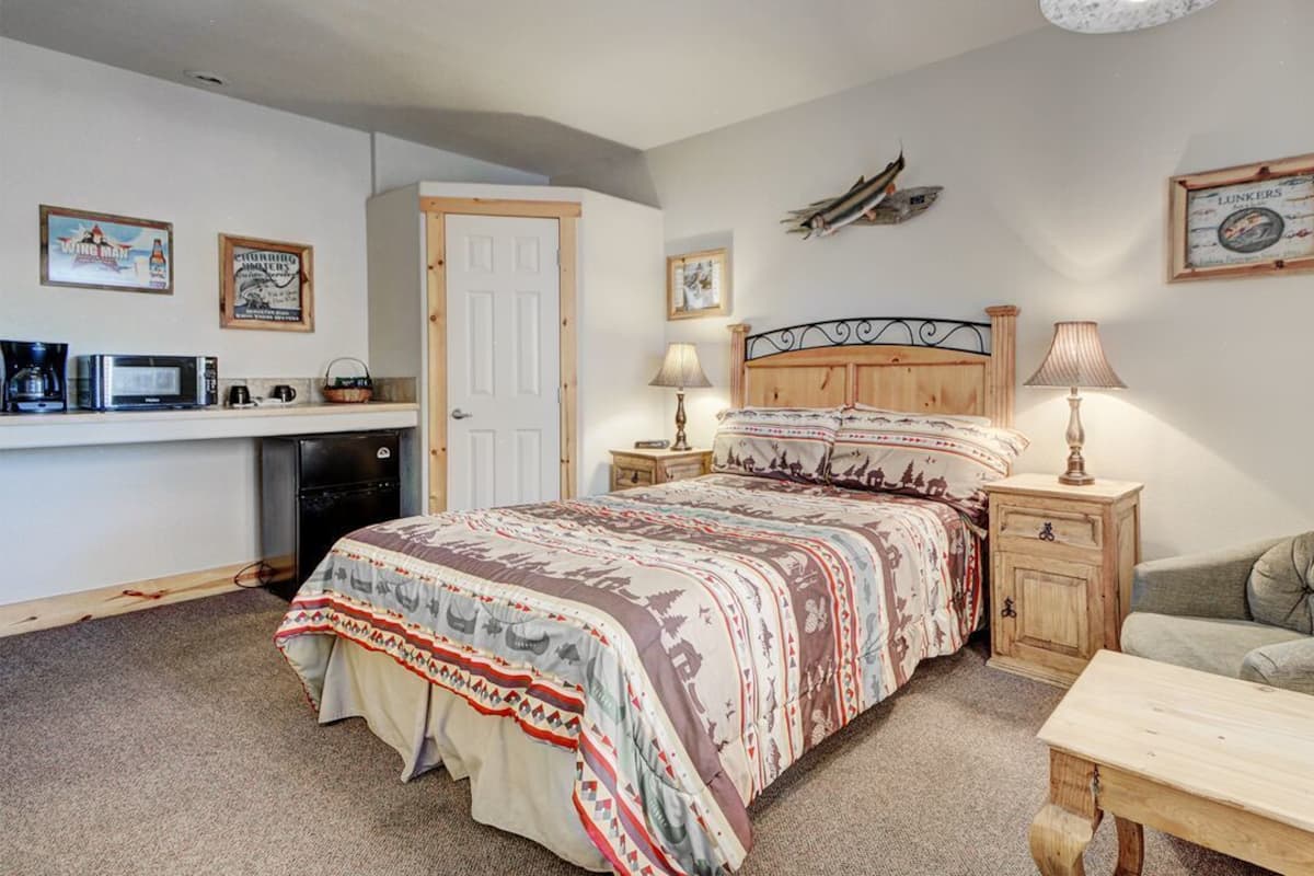 A bedroom with a bed, bedside tables, a chair, a desk, and a kitchenette.
