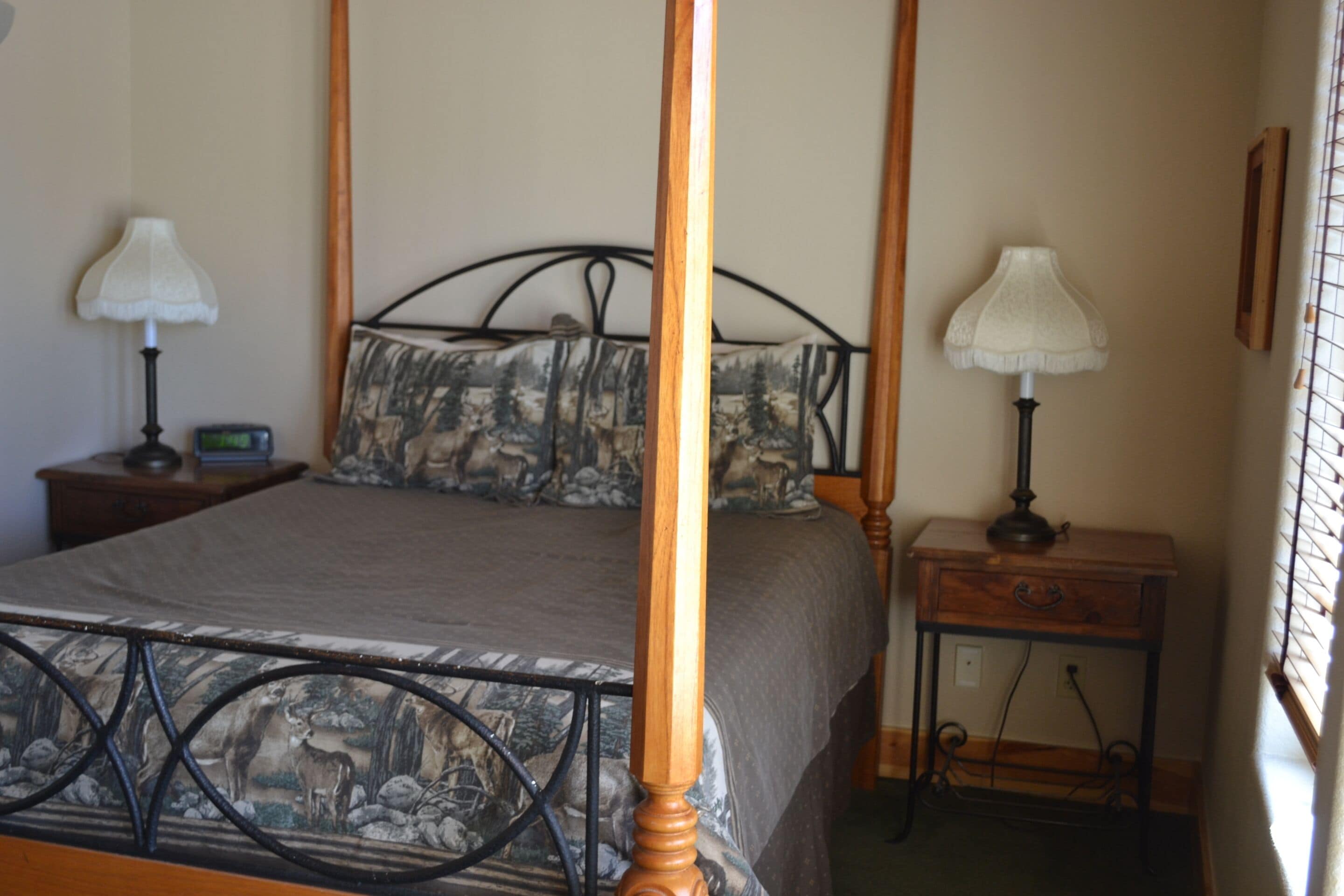 Un lit à baldaquin avec une couvre-lit aux motifs forestiers, deux tables de chevet avec des lampes et une petite table de nuit avec une horloge.