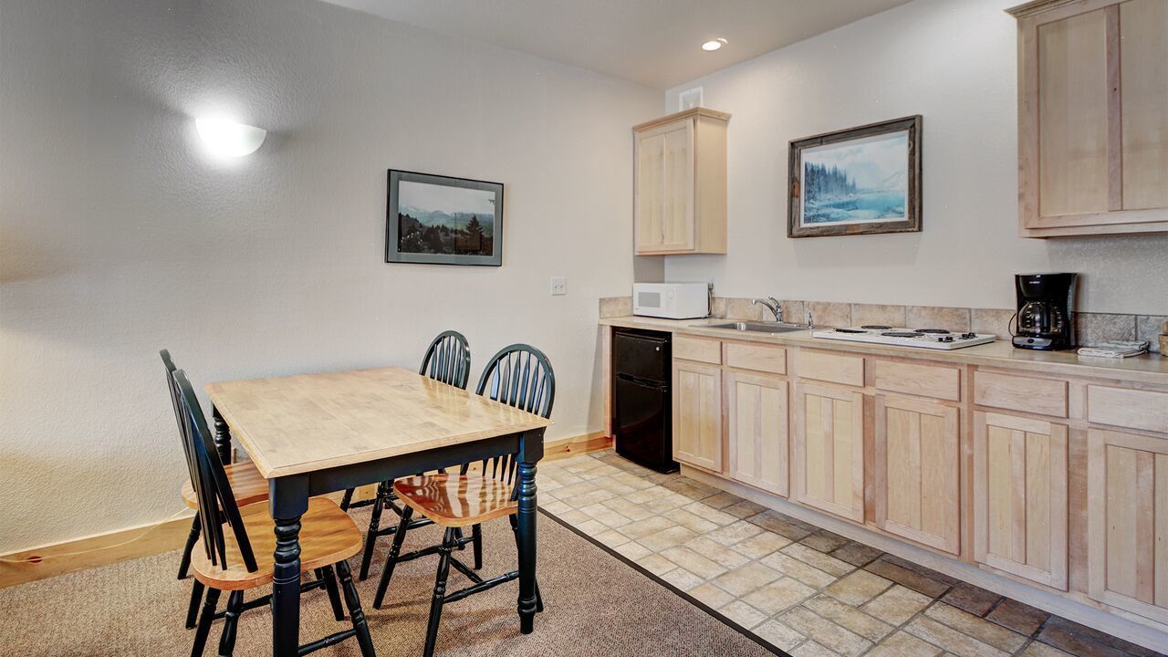 A compact kitchen with a dining table, chairs, a microwave, a coffee maker, and wooden cabinets.