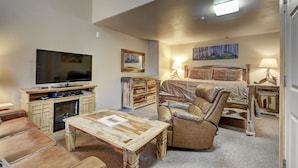 A cozy hotel room with a large bed, a flat-screen TV, a wooden coffee table, and a leather armchair. - Eagle Fire Lodge & Cabins (Woodland Park)