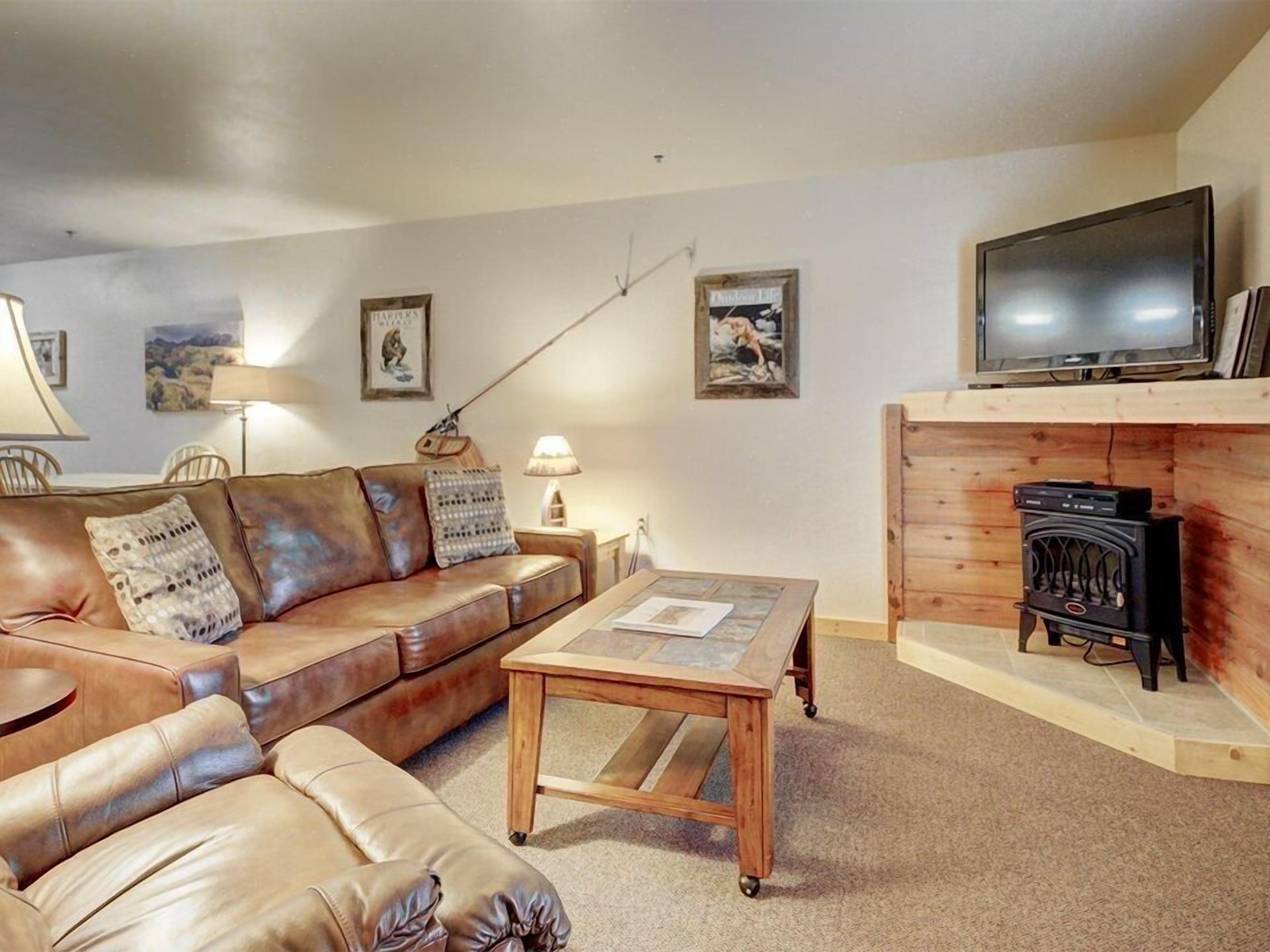 A living room with a leather sofa, a wooden coffee table, a television, and a fireplace.