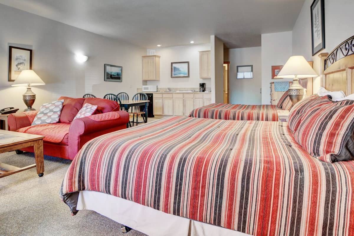 A hotel room with two beds, a sofa, a dining table, and a kitchenette.