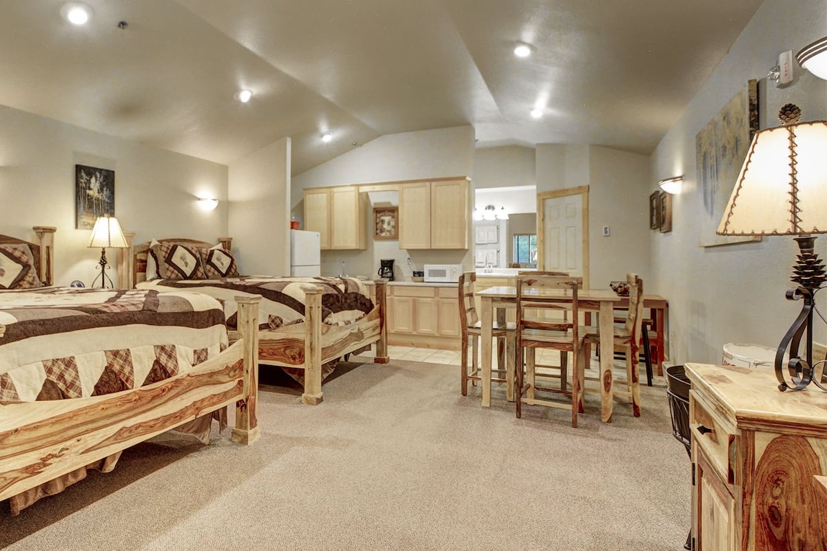 A bedroom with two wooden beds, a desk, and a kitchenette.