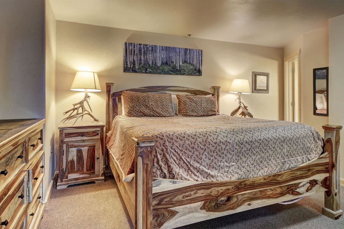 A bedroom with a wooden bed, two bedside tables with lamps, a dresser, and a painting on the wall.