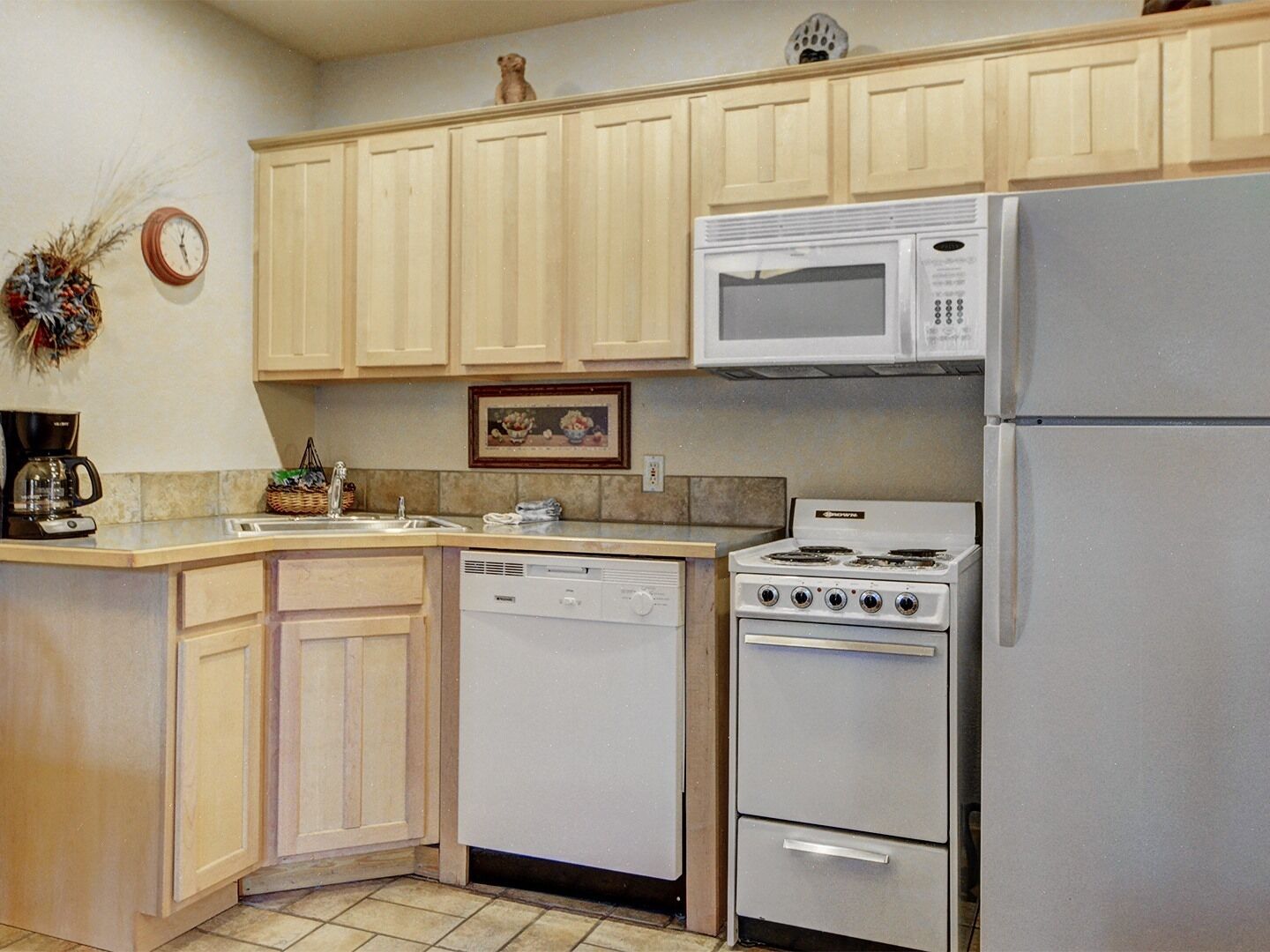 Une cuisine avec des meubles de couleur bois clair, un micro-ondes blanc, un lave-vaisselle blanc et une cuisinière blanche.