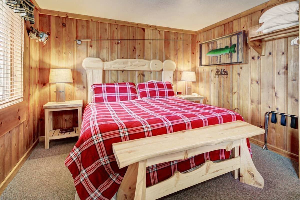 A wooden room with a bed, two bedside tables, a bench, and a wardrobe.