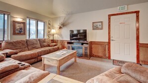 A living room with a brown leather sofa, a wooden coffee table, a television, and a fireplace. - Eagle Fire Lodge & Cabins (Woodland Park)