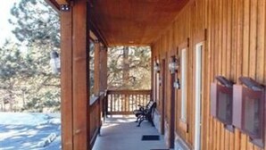 A wooden covered porch with a bench, a view of trees, and a clear sky. - Eagle Fire Lodge & Cabins (Woodland Park)