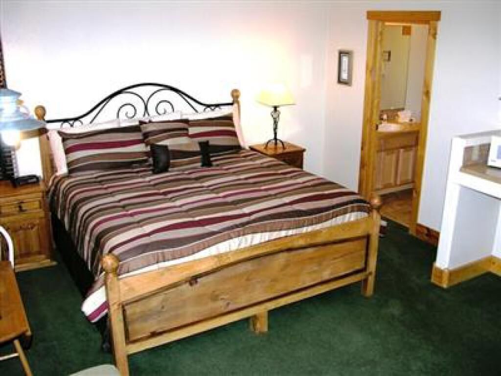 Ein hölzernes Bett mit gestreifter Bettdecke, ein Nachttisch mit Lampe, ein Holzschrank und ein Spiegel an der Wand.