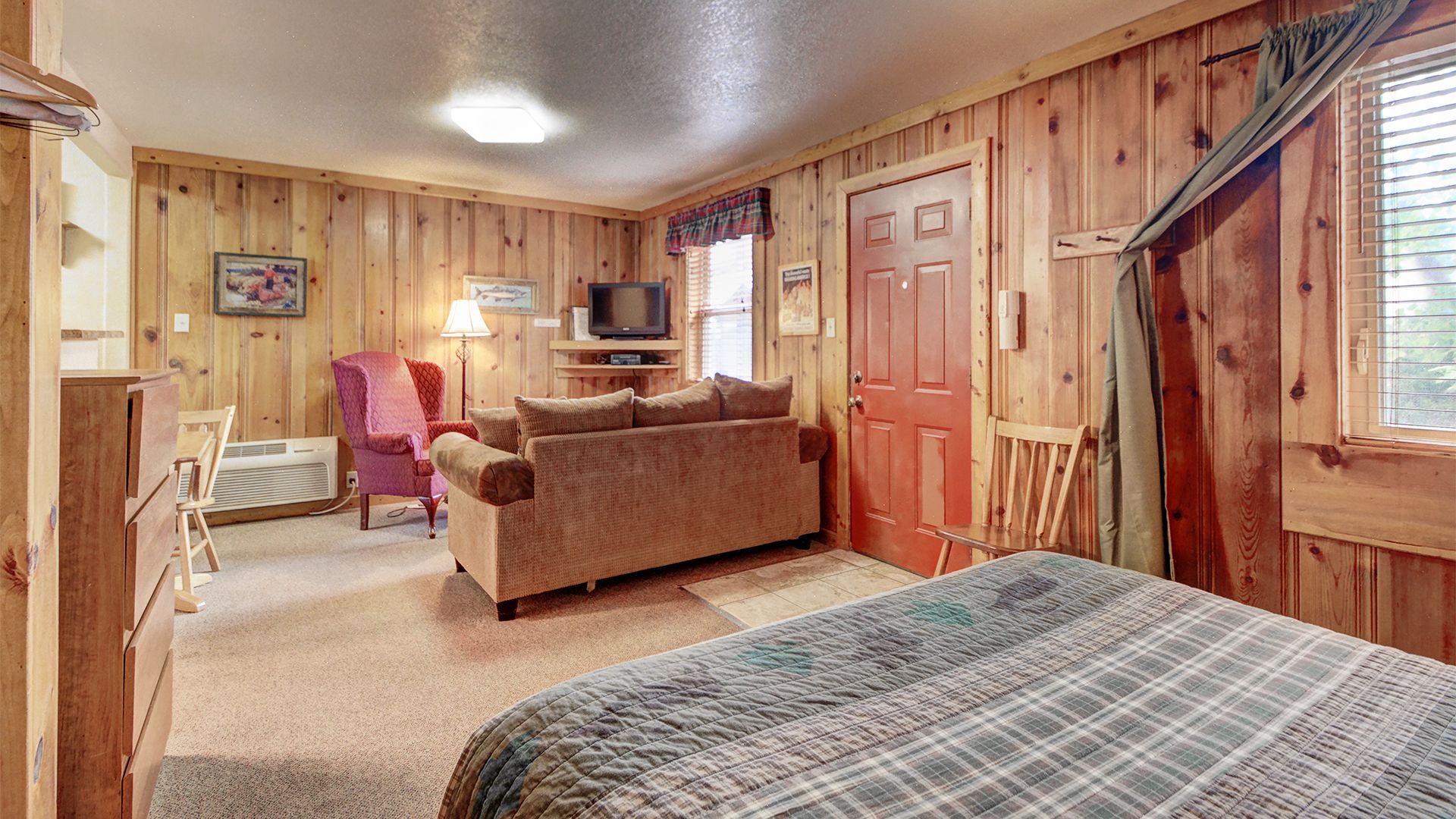 Ein gemütliches Zimmer mit Holzwänden, einer Couch, einem Sessel, einem Fernseher und einem Bett.
