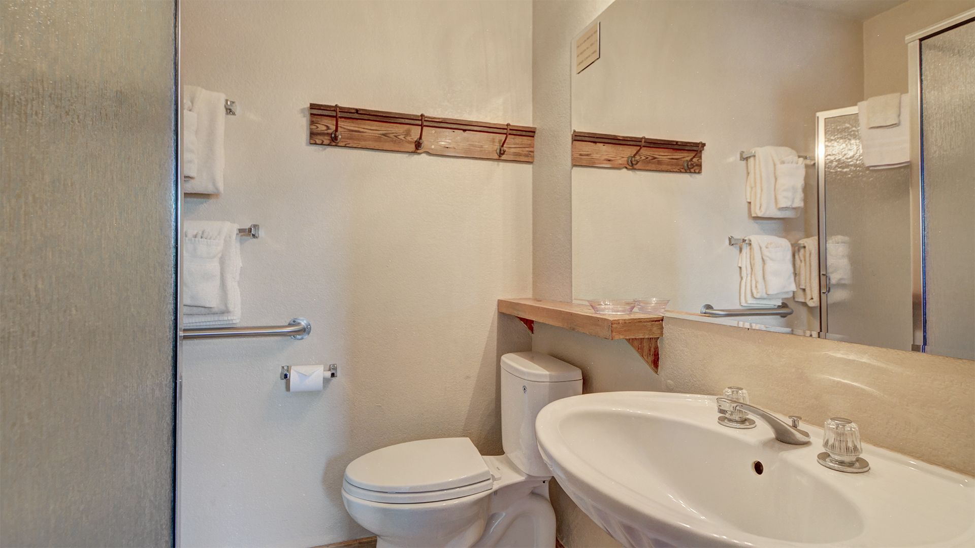 Un baño con inodoro, lavamanos y espejo. Hay toallas colgadas en ganchos y una zona de ducha.