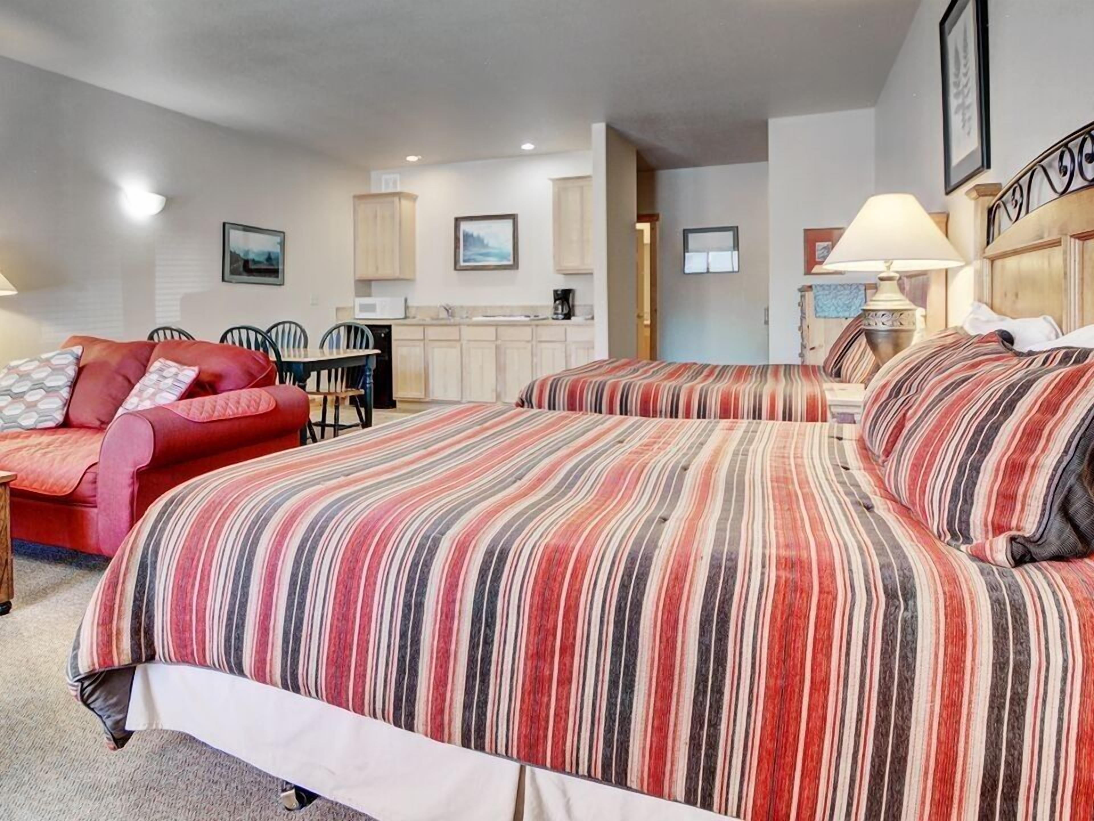 Una habitación de hotel con dos camas, un sofá rojo, una mesa de comedor y una kitchenette.