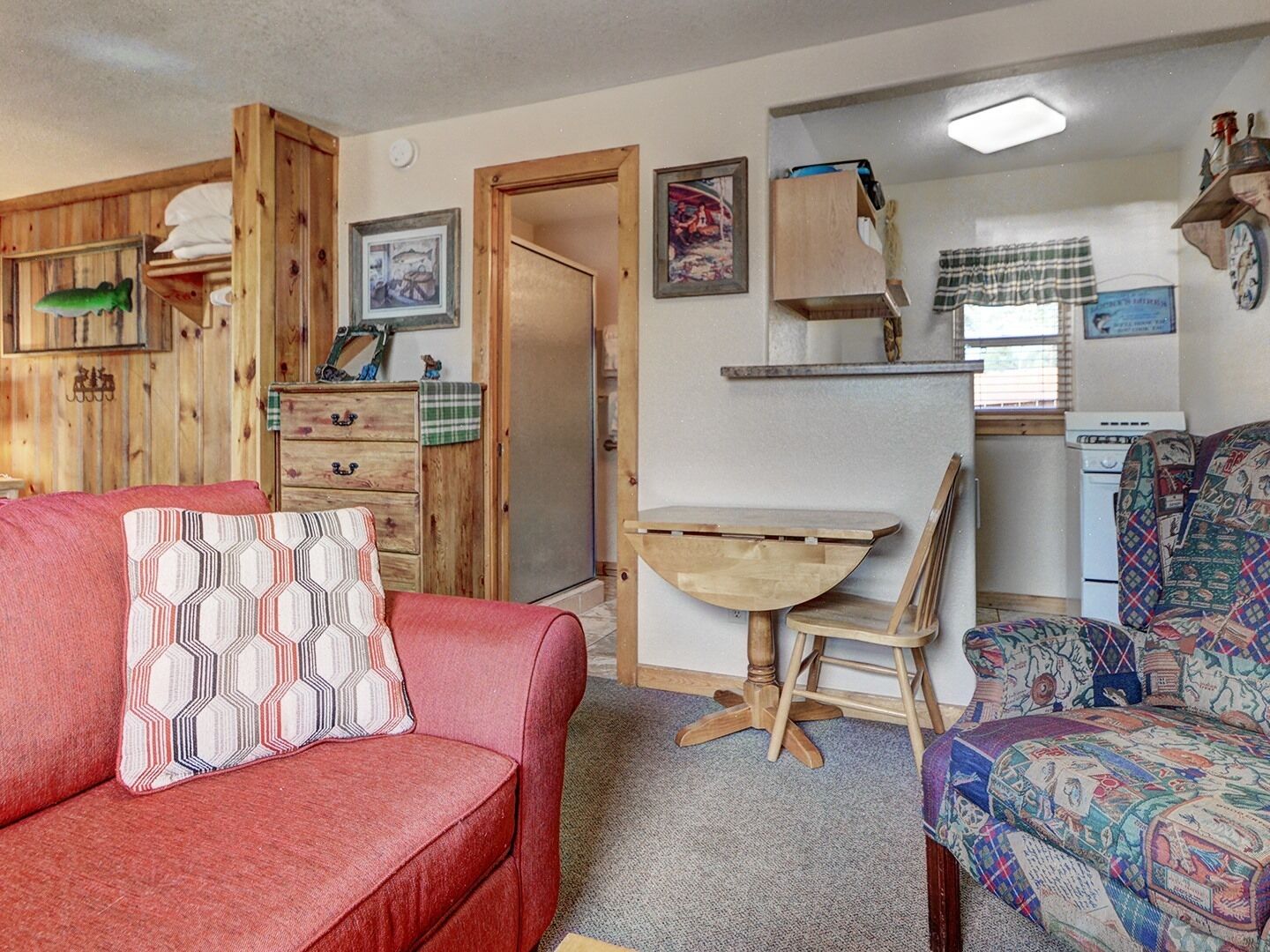 Een gezellige kamer met een rode bank, een gestreept fauteuil, een houten dressoir en een klein tafeltje.