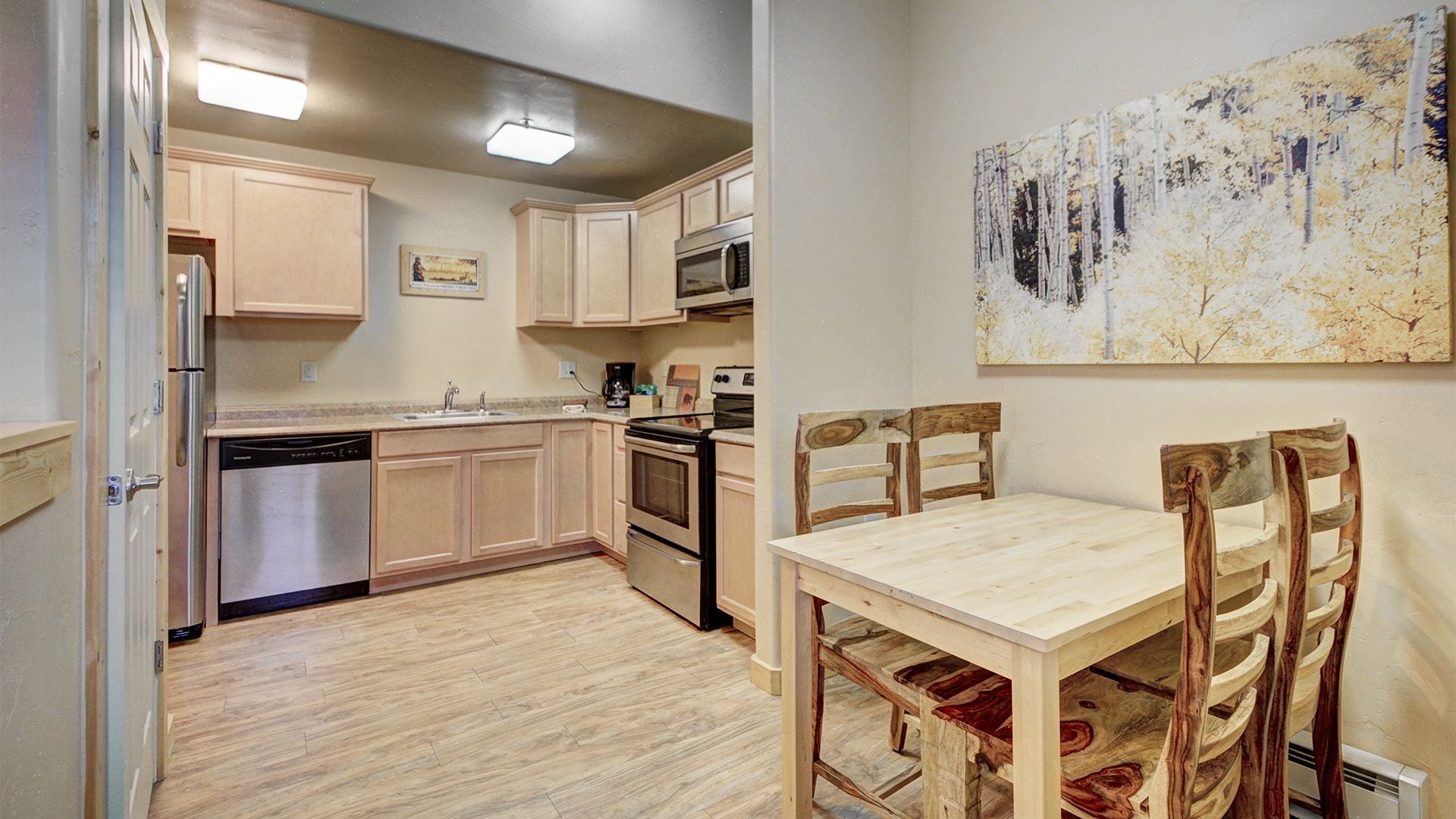 A compact kitchen with wooden cabinets, stainless steel appliances, and a dining area with a wooden table and chairs.