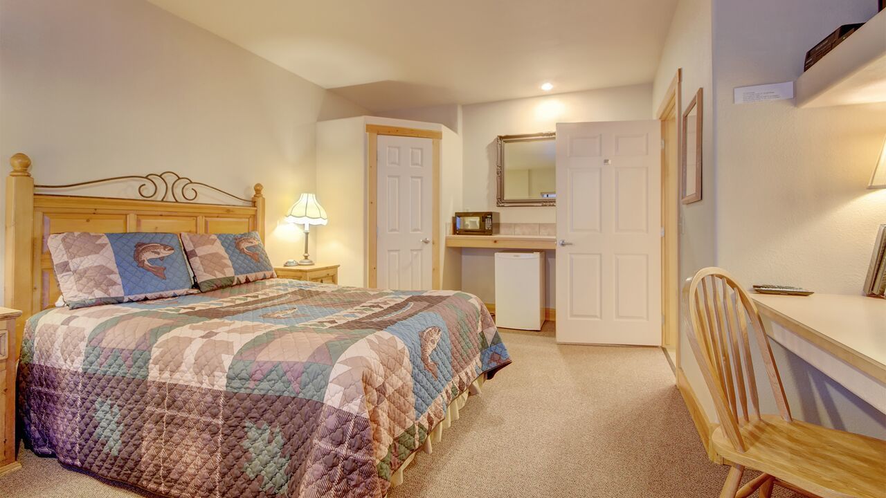 A bedroom with a bed, bedside table, lamp, and a desk with a chair.