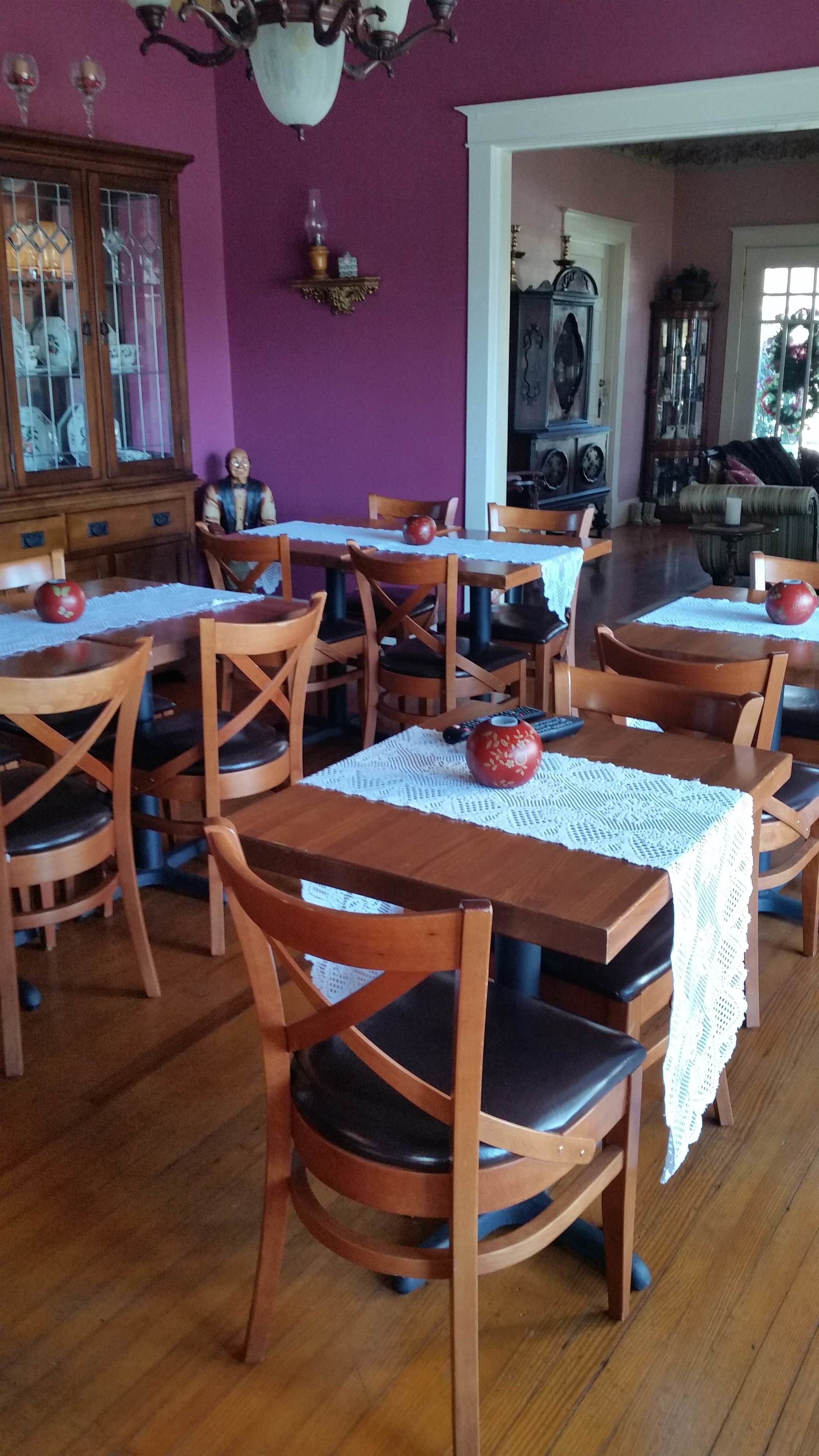 A dining area with wooden tables and chairs, a purple wall, and a chandelier.