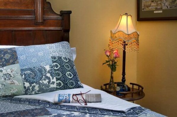 A neatly made bed with patterned pillows, a bedside lamp with a floral design, and a small table with a vase of flowers.